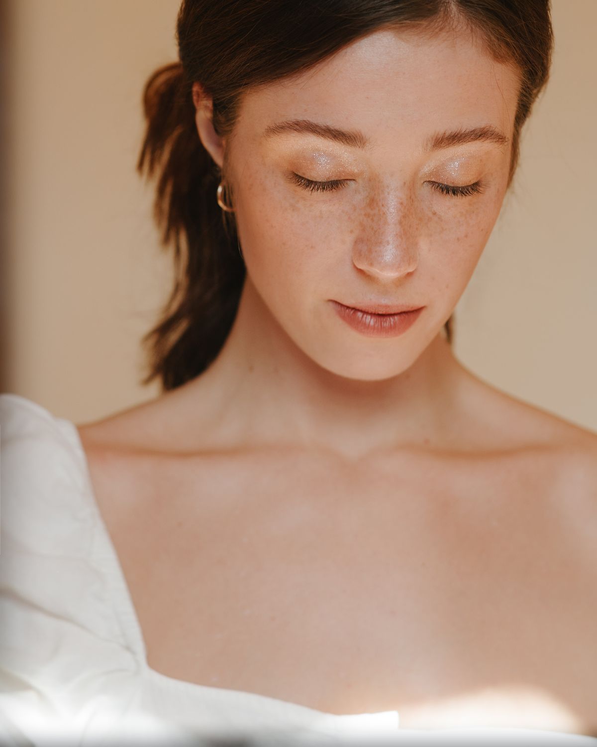 Mujer de piel clara con pecas y los ojos cerrados bajo luz natural