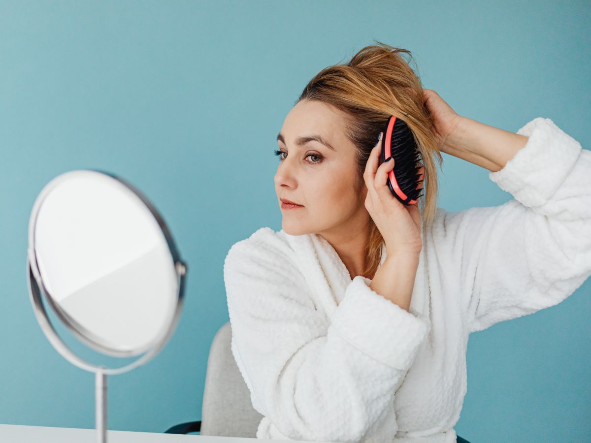 Mujer cepillándose el pelo frente al espejo