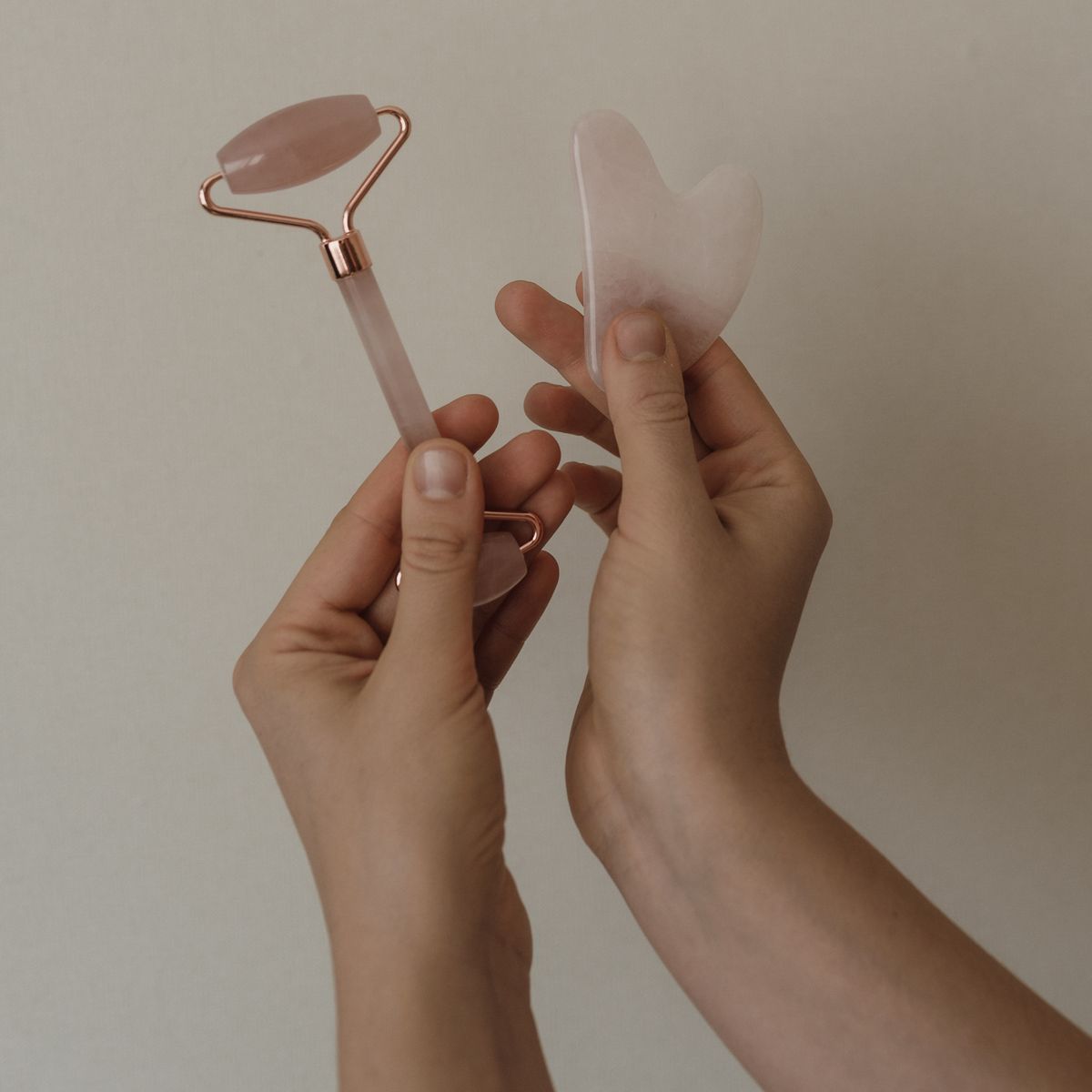 Manos sosteniendo un rodillo facial y una gua sha de cuarzo